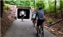 Three bike riders on a concrete path going into a tunnel. 