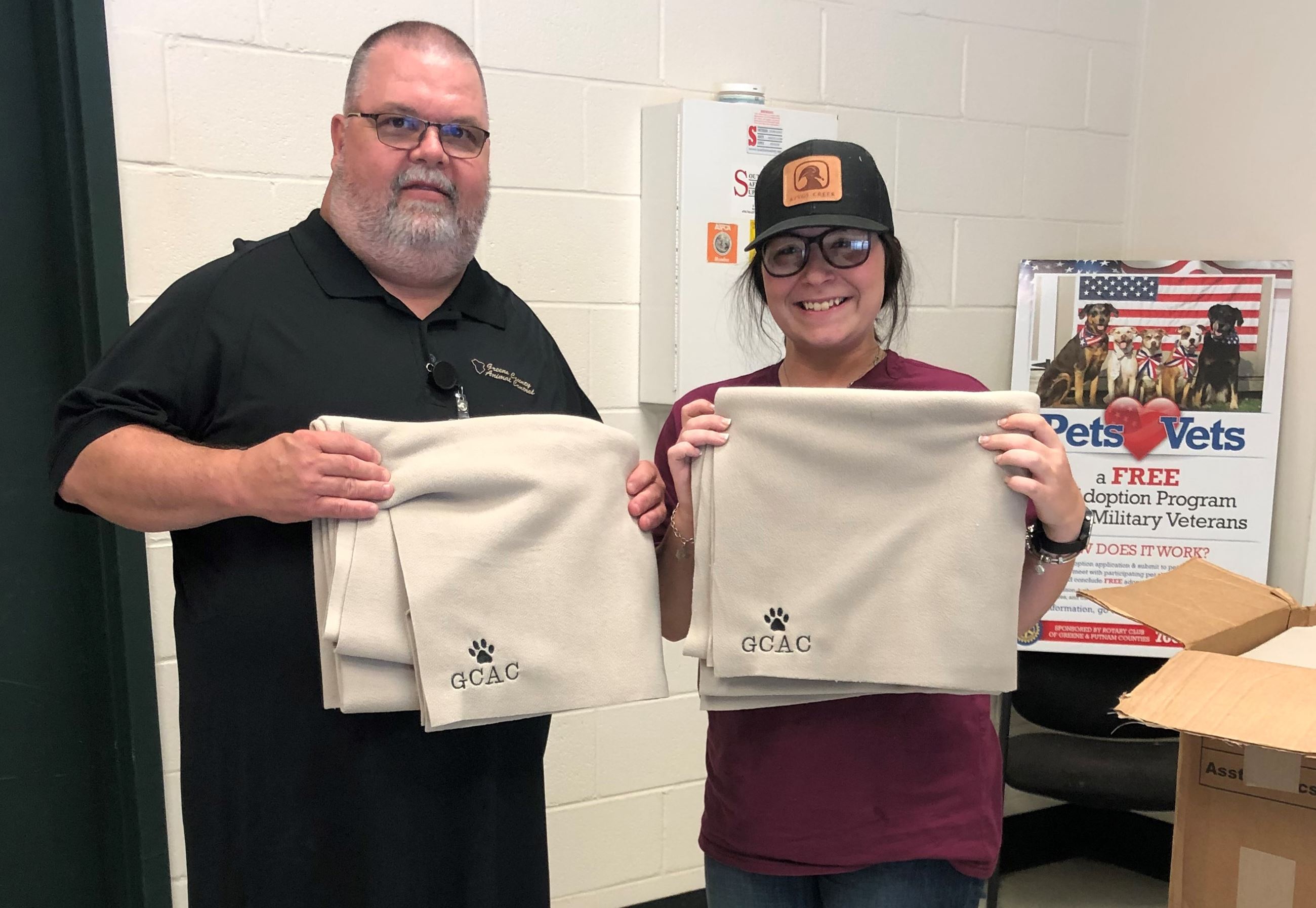 Man and woman each holding a blanket with GCAC and an animal paw embroidered on it.