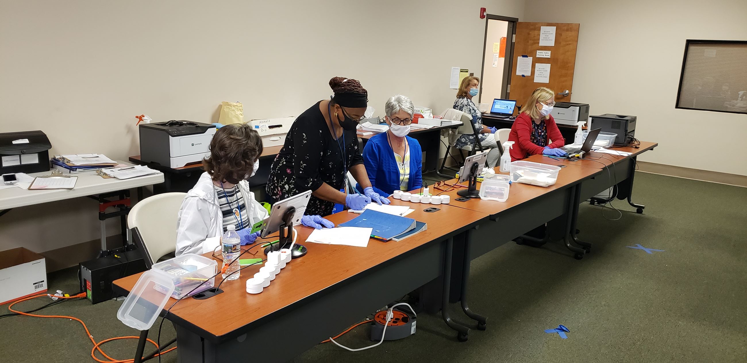 Five ladies wearing COVID masks working behind a desk.  